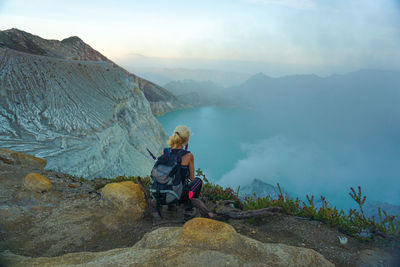 Woman looking at view while sitting on mountain against sky