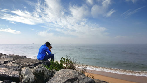 Rear view of man photographing by sea against sky