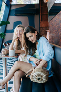 A woman is looking for cosmetics in a wicker bag while sitting in a cafe with a girlfriend.