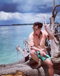 Full length of young man sitting at sea against sky