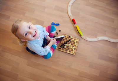 High angle portrait of smiling girl sitting by chessboard at home