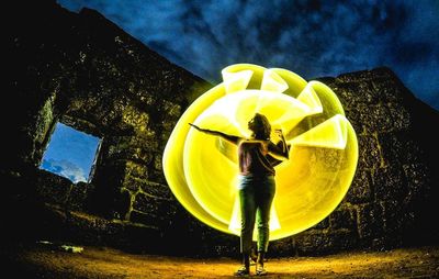 Man with yellow umbrella against sky at night