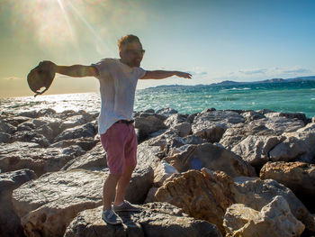 Man standing on rock by sea against sky