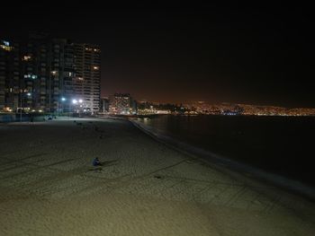 Illuminated cityscape by sea against sky at night