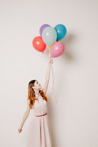 Low angle view of girl holding balloons against white background