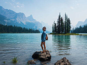 Woman standing on rock by lake against mountains