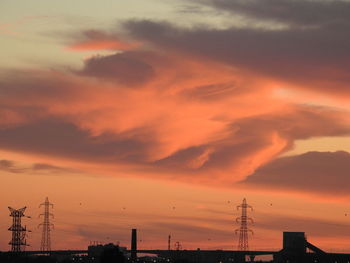 Electricity pylons against sky during sunset