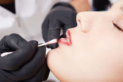 Cropped hand of beautician applying lipstick on woman lips at spa