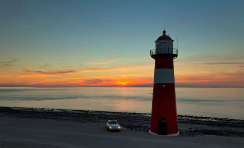 Car by lighthouse against sky during sunset