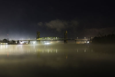 Illuminated bridge over river against sky at night