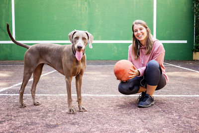 Portrait of smiling woman holding ball with dog outdoors