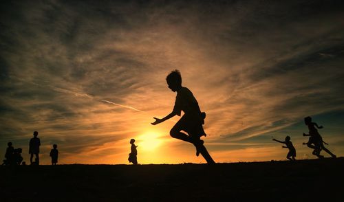 Silhouette men playing soccer against sky during sunset