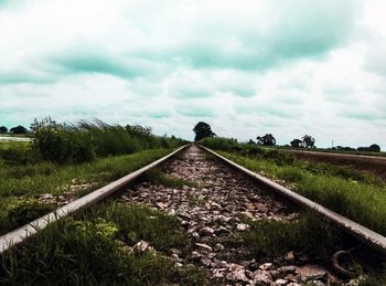 Railroad track amidst field against cloudy sky