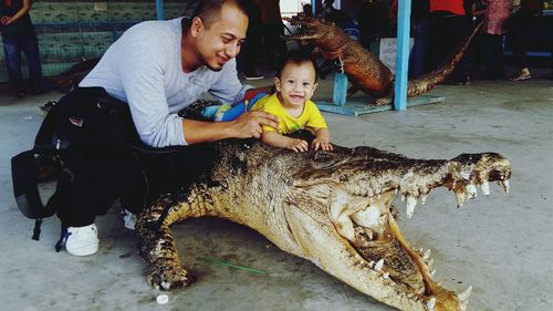 Father with cheerful son lying on crocodile taxidermy
