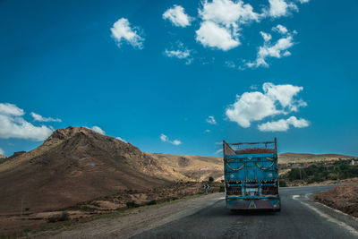 Road leading towards mountain against blue sky