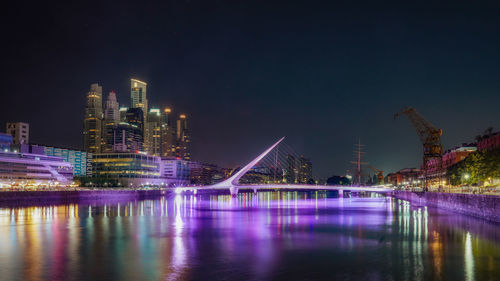 Illuminated city by river against sky at night