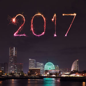 Firework display over illuminated buildings against sky at night
