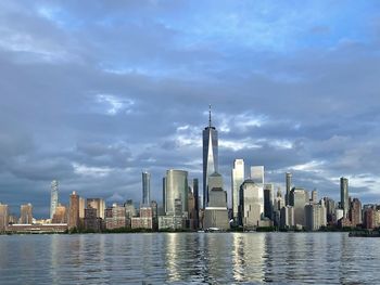 Buildings in city at waterfront against cloudy sky