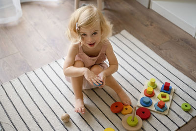 Smiling girl looking at camera playing with eco wooden toys sitting on carpet.happy adorable toddler