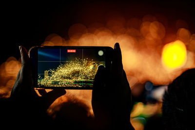 Cropped hand of woman using mobile phone to capture molten iron flower show