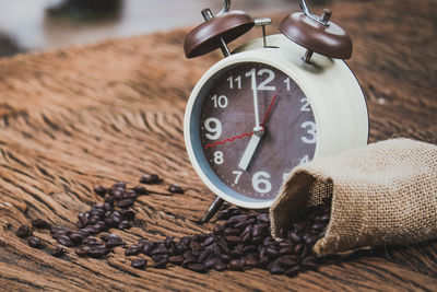 A brown alarm clock and coffee beans in a sack bag, on old wood table
