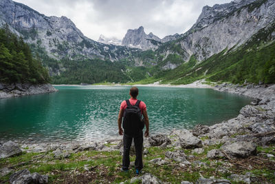 Rear view of man standing on lake against mountains