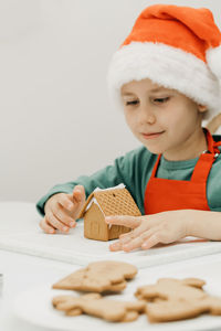 A cute boy on new year's eve and christmas makes a ginger house in the kitchen in a santa hat.