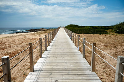 Wooden walkway leading towards sea against sky