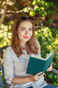 Portrait of beautiful young woman reading book while sitting in park