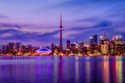 Illuminated buildings in city against cloudy sky