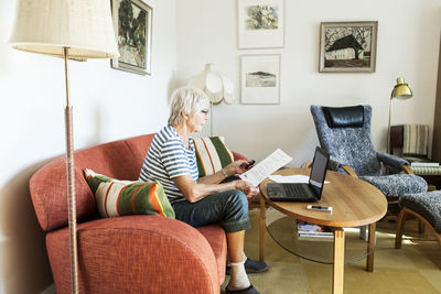 Senior woman analyzing document while using laptop at home