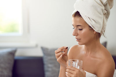 Young woman wearing bathrobe taking medicine while sitting on sofa at home