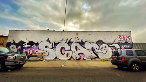 Graffiti on wall by road against sky in city