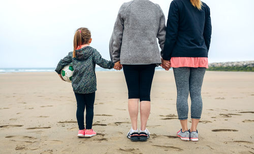 Rear view of woman standing with mother and daughter at beach against sky