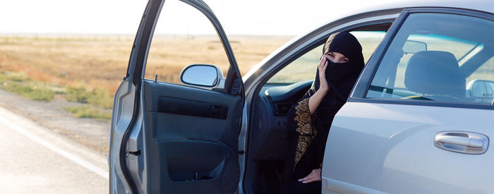 Islamic woman sitting in the car with the front door wide open.