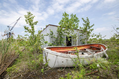 Abandoned boat by cottage amidst plants against sky