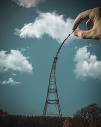 Low angle view of hand holding tower against sky