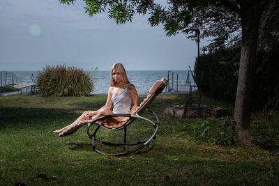 Portrait of young woman sitting on lounge chair against sea 