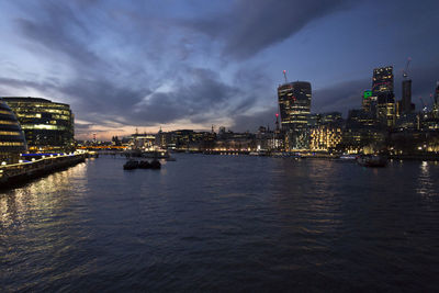 Illuminated city by river against sky