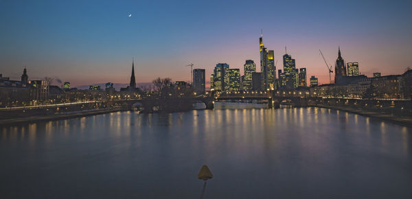 View of river against illuminated buildings during sunset