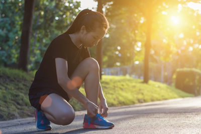 Full length of woman tying shoelace on road during sunny day