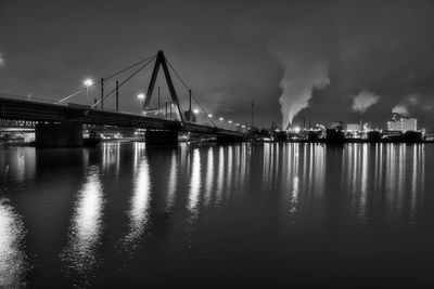 Illuminated highway bridge over a big river at night with industrial buildings in the background