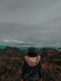 Rear view of man standing on mountain against sky