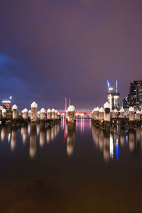 Illuminated buildings by sea against sky at night