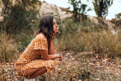 Side view of young woman crouching on on land at forest