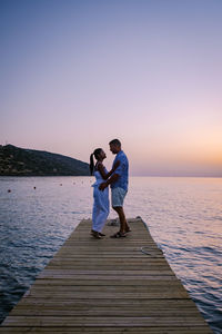 Rear view of couple on pier over sea against sky during sunset