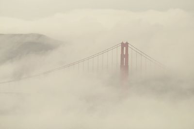 Suspension bridge in foggy weather against sky