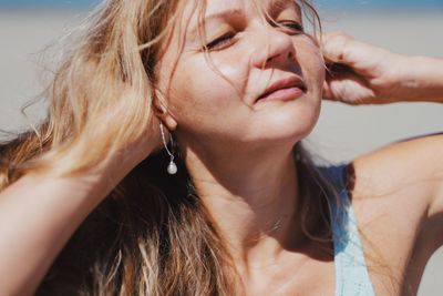 Portrait of a mature blond woman touching her hair and sunbathing with closed eyes