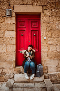 Close-up of woman using smart phone while sitting by door