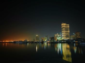 Illuminated city by river against sky at night